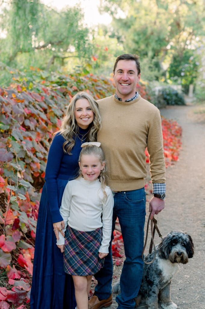 A family of 3 with their dog taking fall family photos on a trail.