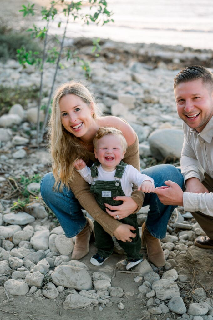 A family of three taking family photos on the beach in the fall.
