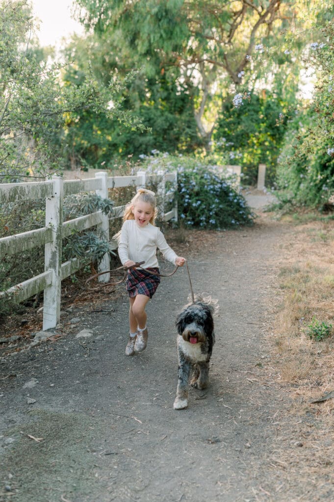 A little girl running and laughing with her dog on a beautiful trail.