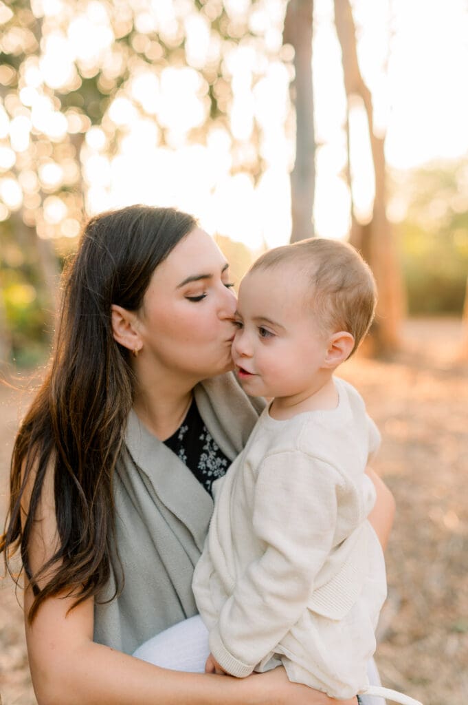 A mom kisses her baby girl on the cheek.