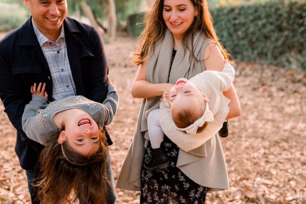A mom and dad holding their young daughters while they laugh during fall family photos.