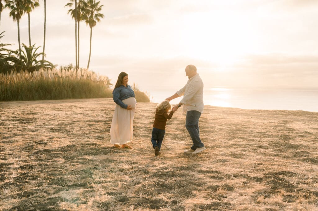 A family holds hands and dances on a cliff at sunset while taking fall family photos.