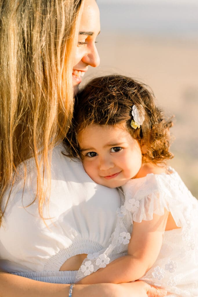 A little girl smiles in her mom's arms as they laugh and snuggle.