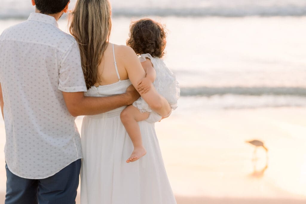 A family looking out at the sunset during a family photography session on the beach.