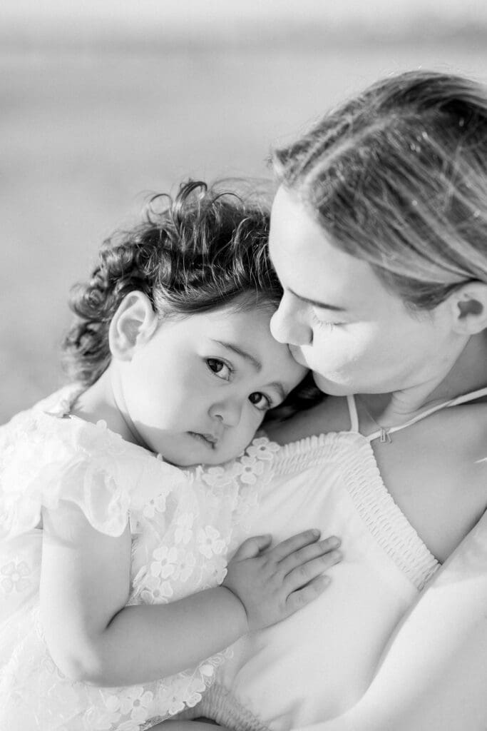 A mom holding her young daughter while being photographed by a Manhattan Beach family photographer.