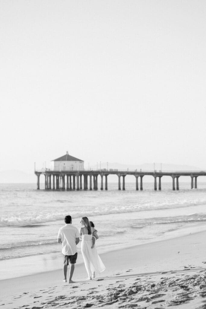 A family walking on the beach with the Manhattan Beach pier in the background.