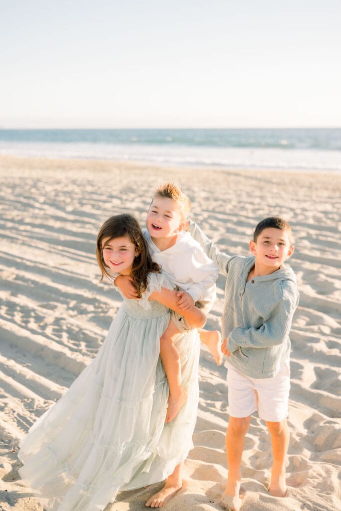 Siblings doing piggy back rides during their family beach photo session in the South Bay.