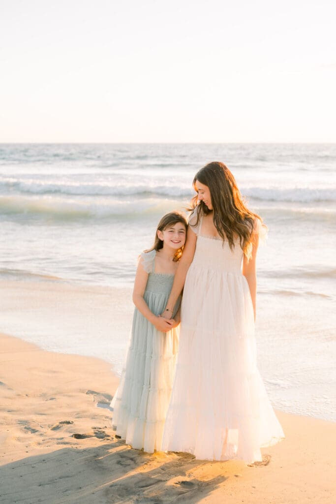 A mom and daughter in flowy dresses on the beach taking family photos.