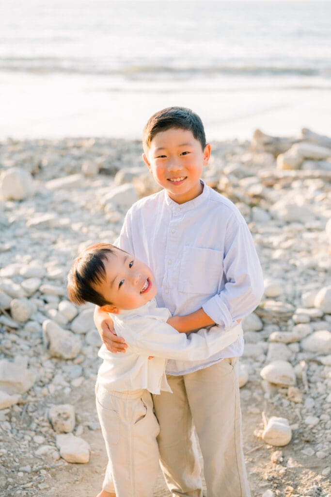 Brothers hugging on the beach taking family photos.