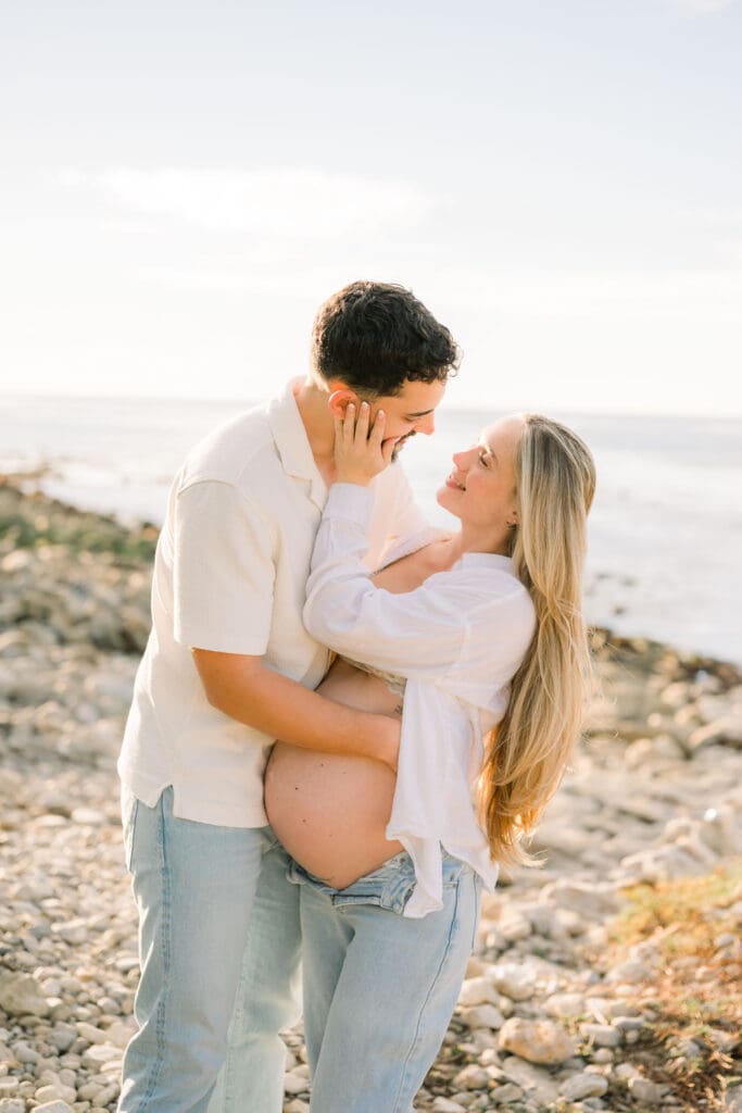 A couple holding each other close as they pose for casual beach maternity photos in the South Bay.