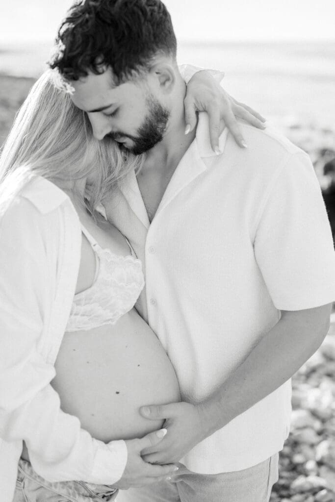 A man holds his pregnant wife as they take maternity photos.