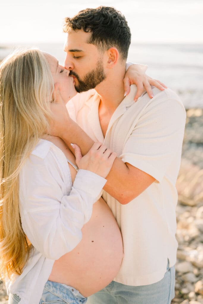 A pregnant woman kisses her husband during their maternity photo session at the beach.