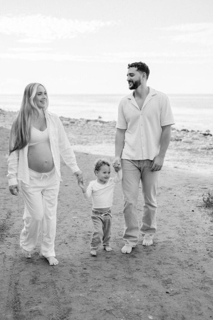 A family of 3 walking on the beach during a maternity photo shoot.