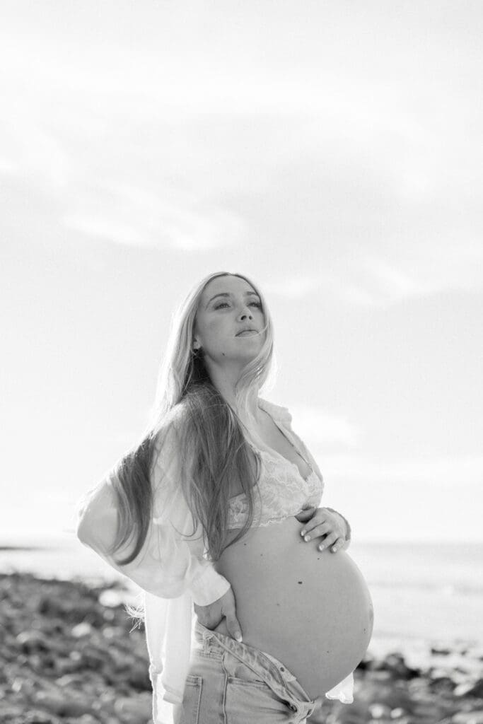 A black and white photo of a pregnant woman on the beach taking maternity photos.