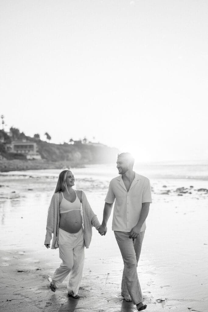 A pregnant couple walking along the ocean.
