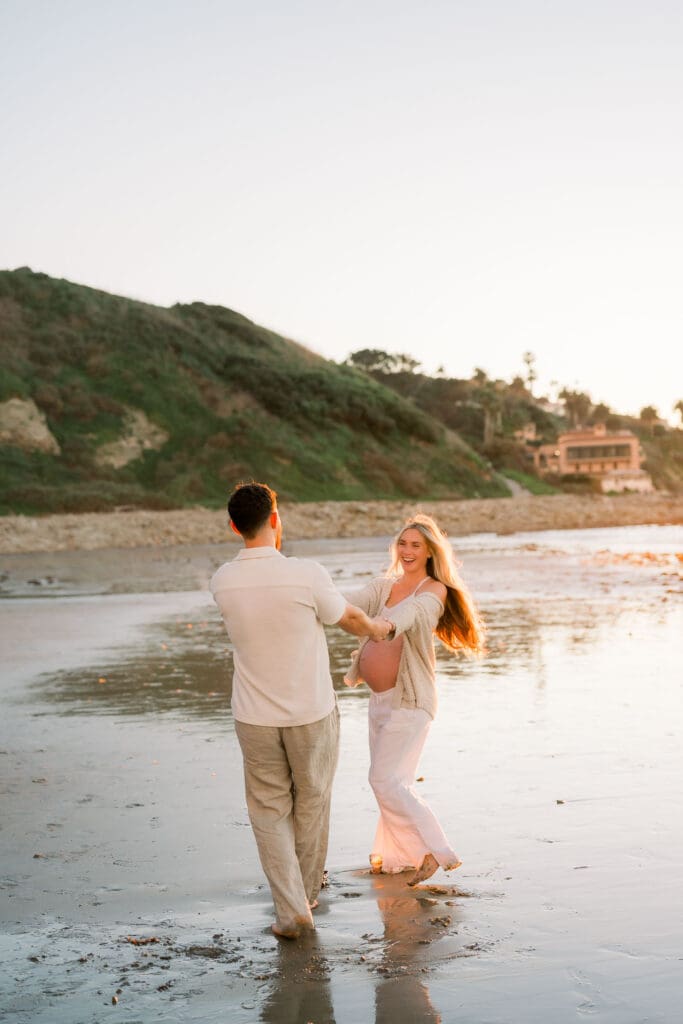 Sunset maternity photos of a couple dancing on the sand.