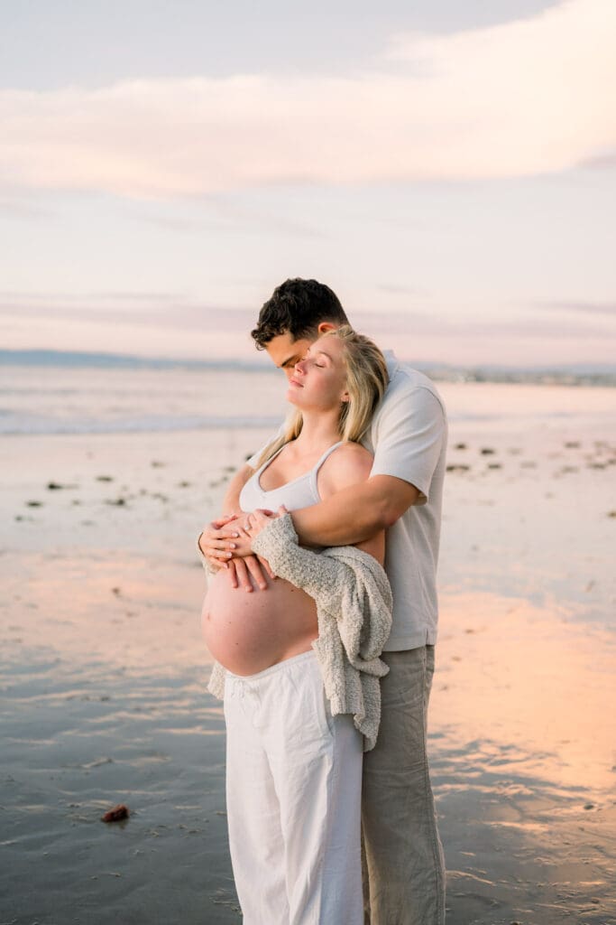 A couple watches the sunset while taking casual beach maternity photos in the South Bay.