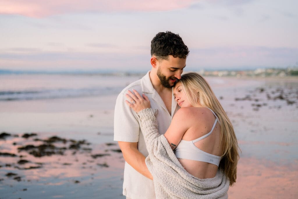 A couple snuggling on the beach with a beautiful blue and pink sky.