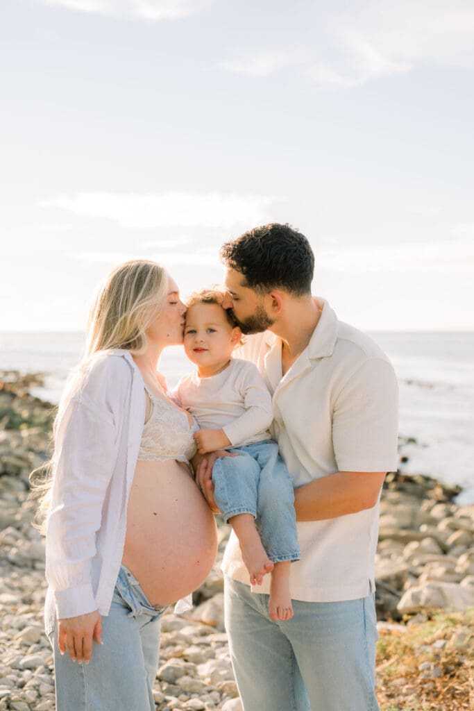 Mom and dad kiss their son's cheeks while posing on a beach.
