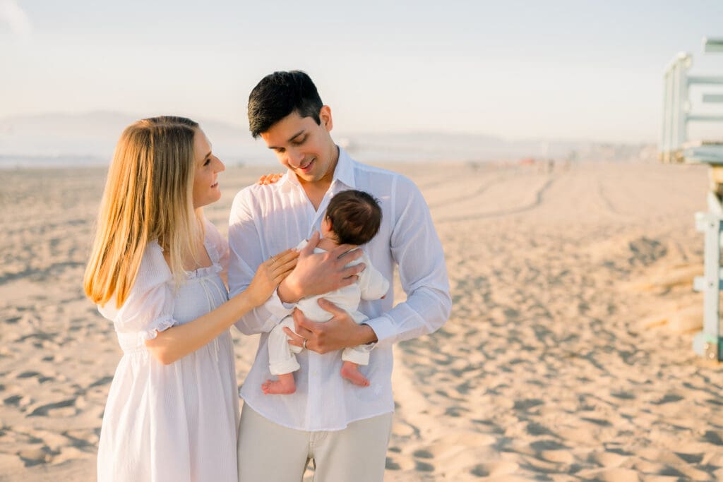 A family poses with their new baby while taking newborn photos on the beach.