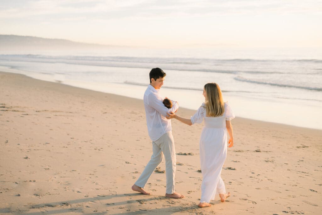 A new family walking on the beach at sunset wearing white linen clothes.