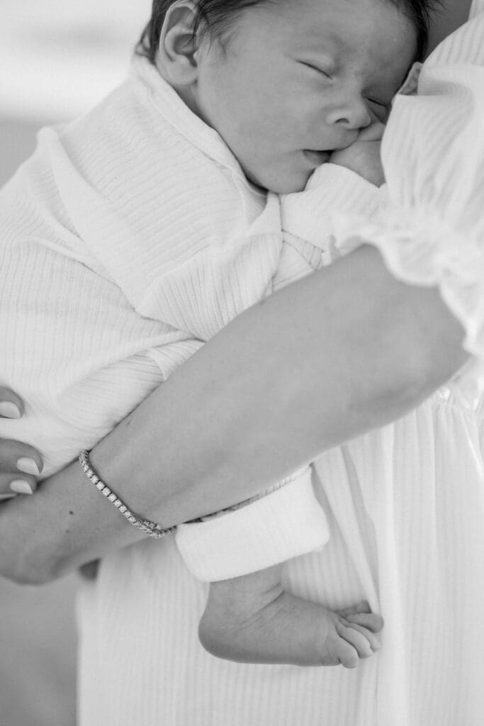 A newborn baby sleeps in mom's arms while a Hermosa Beach newborn photographer takes their photo.