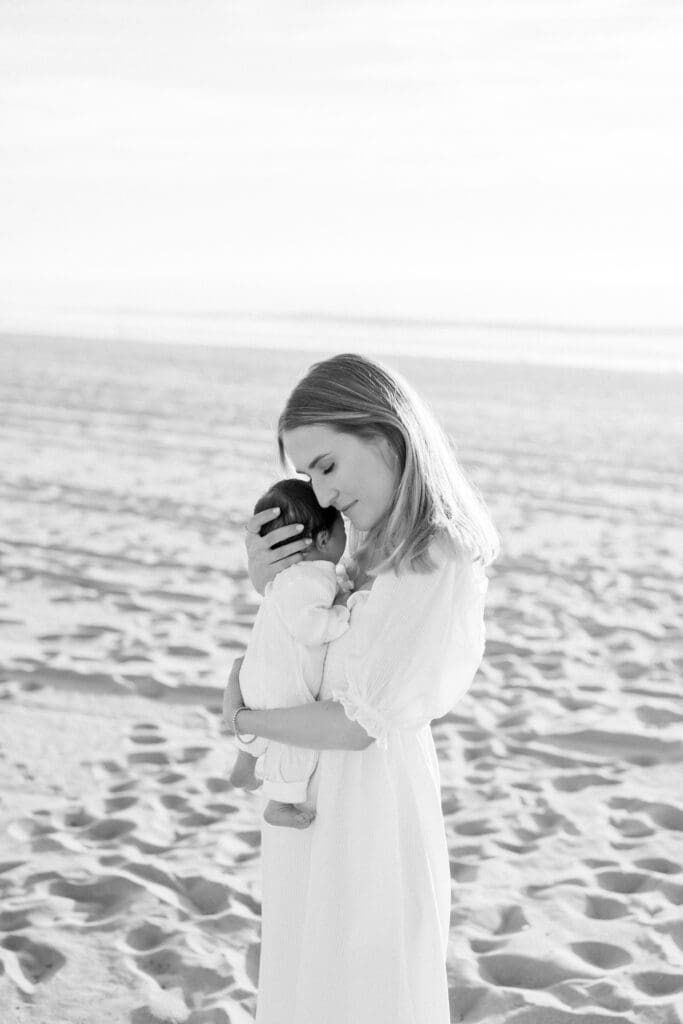 A black and white photo of a mom snuggling her newborn baby during a newborn photo session on the beach in Hermosa Beach.