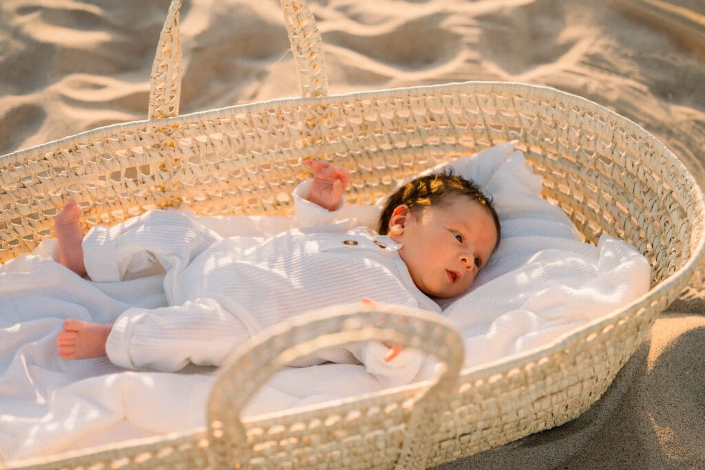 A newborn baby in a wicker moses basket on the beach.