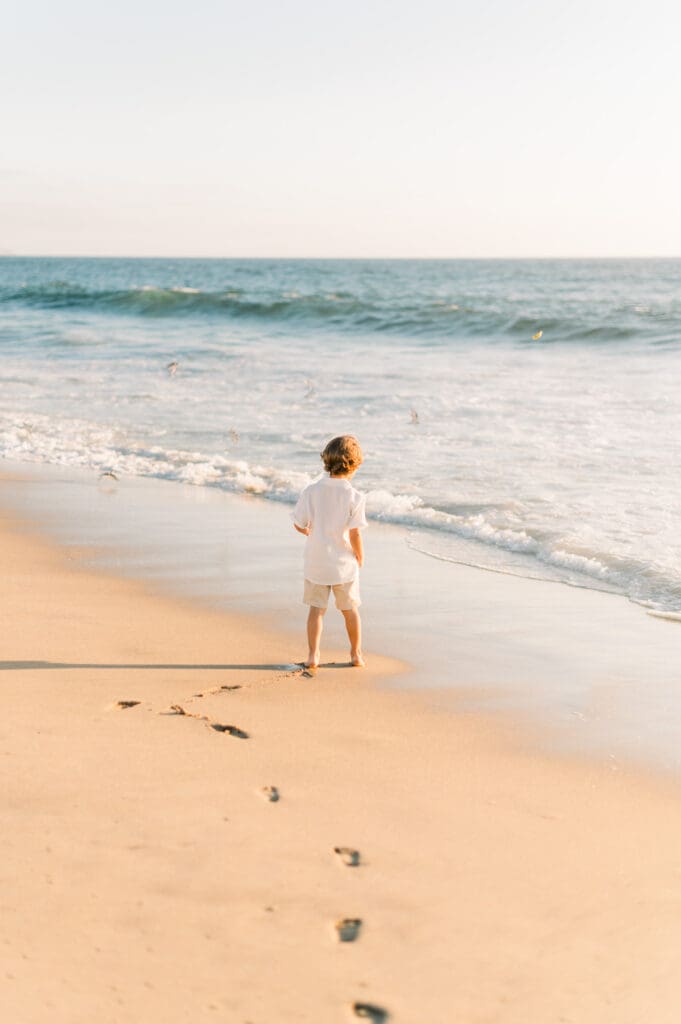 A little boy and his footprints in the sand on the beach.