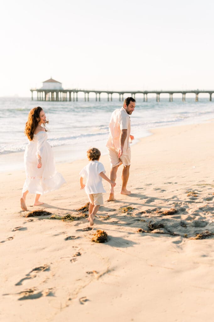 A mom, dad, and little boy running on the beach by the Manhattan Beach Pier.