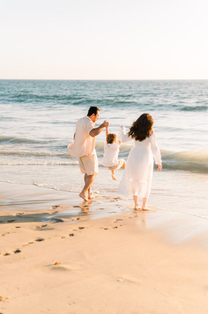 A family playing in the water at the beach while taking maternity photos.