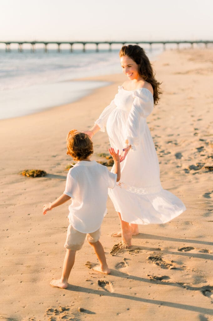 A pregnant mother dances with her son on the beach while taking maternity photos.