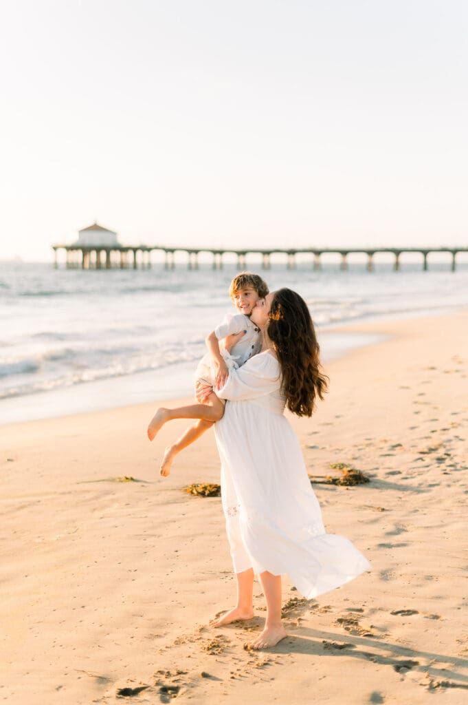 A pregnant mom kisses her son's face while taking maternity photos at the Manhattan Beach pier.