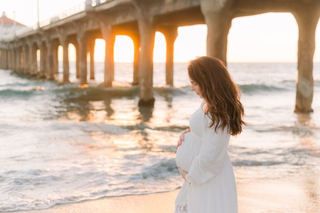 An expecting mom poses for maternity photos at the Manhattan Beach pier during golden hour.