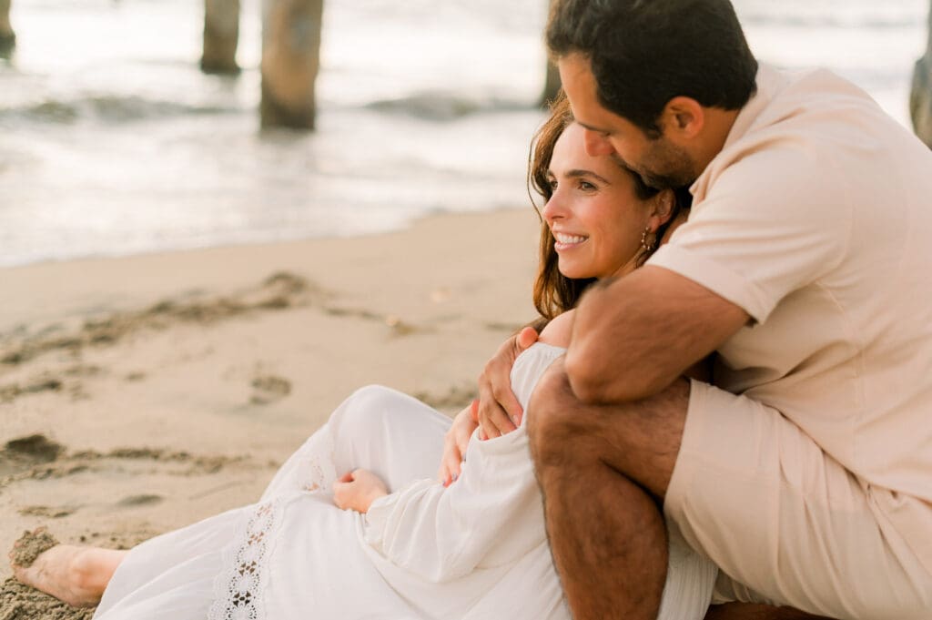 A couple embrace on the beach while taking maternity photos.