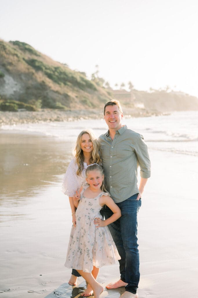 A family of three posing for family photos on the beach.