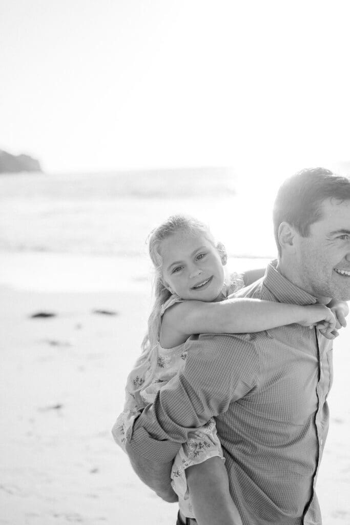 A little girl doing a piggy back ride on her dad's back during a beach family photography session in Los Angeles.