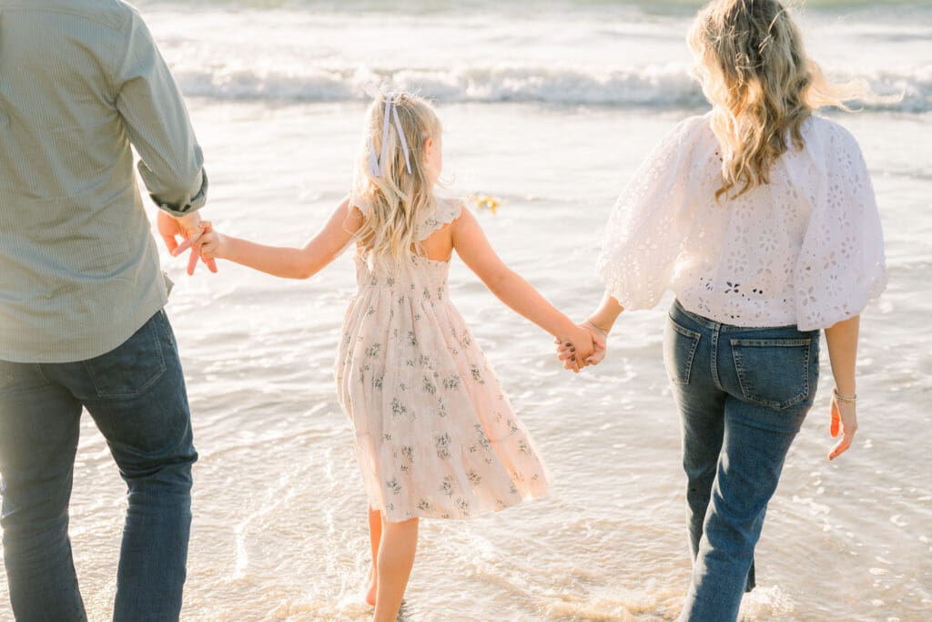 A family holds hands in the ocean together as they take beach family photos in Los Angeles.