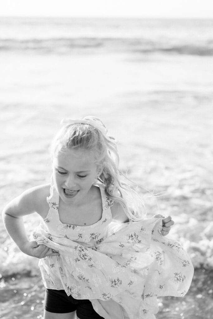 A little girl runs through the ocean in a floral dress.