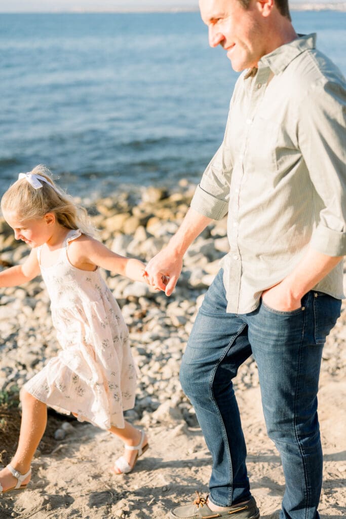 A dad and daughter walking hand in hand during a beach family photography session in Los Angeles.