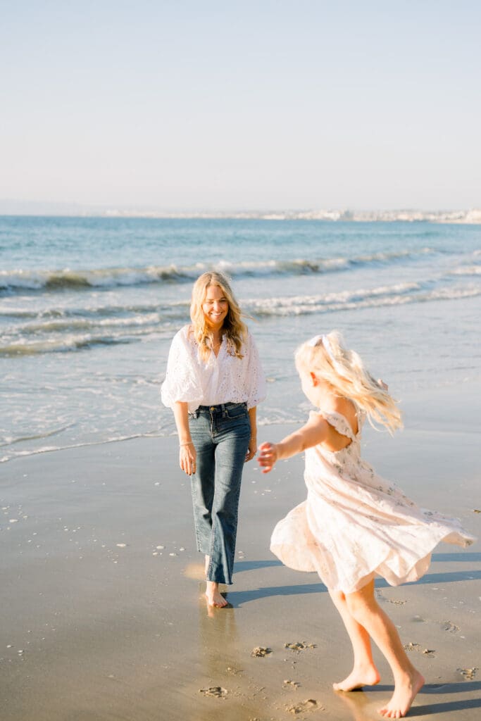 A mom and daughter dance on the beach at sunset while taking beach family photos in Los Angeles.