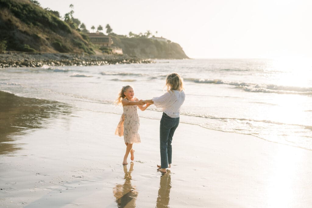 Mom and daughter dance in the ocean at sunset during their beach family photography in Los Angeles.
