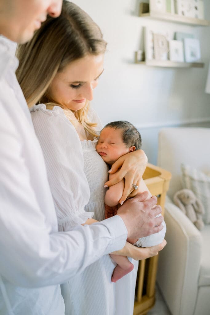 Mom looks lovingly at her newborn baby while he sleeps wearing a diaper.