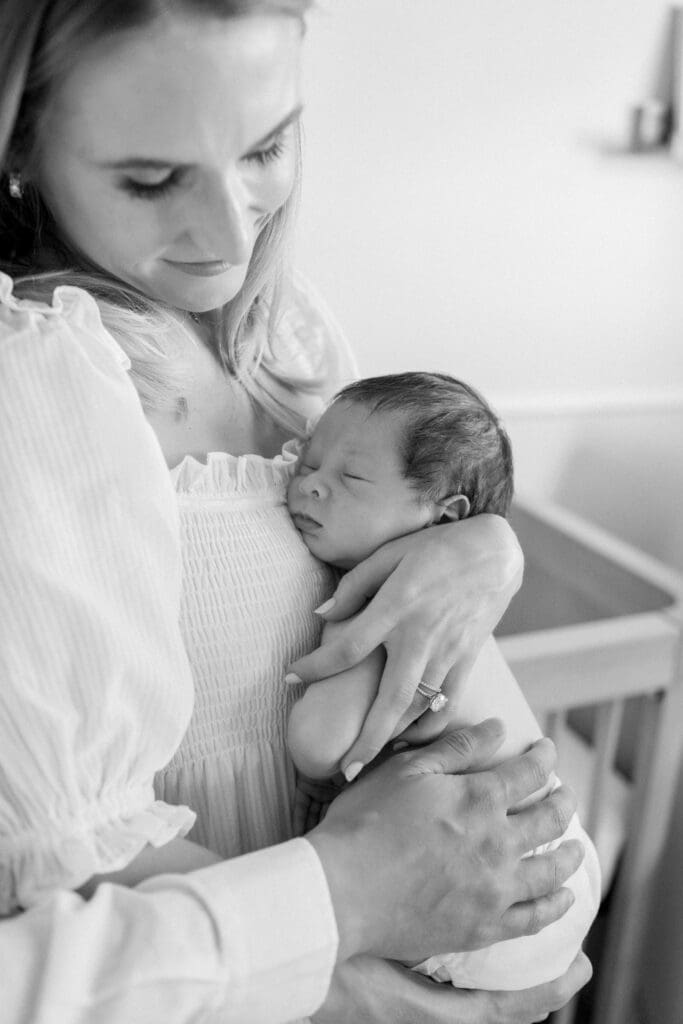 A mom snuggling her newborn baby while he sleeps in her arms during his in home newborn photography session in Los Angeles.