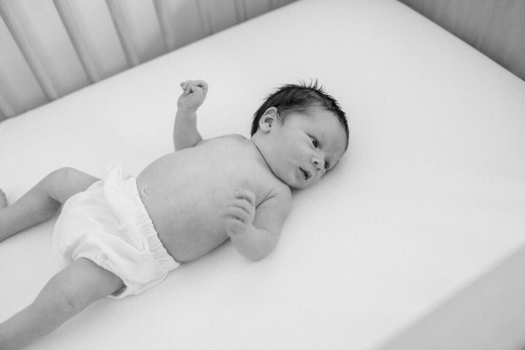 A newborn baby in his diaper laying on his crib and taking newborn photos at home in Los Angeles.