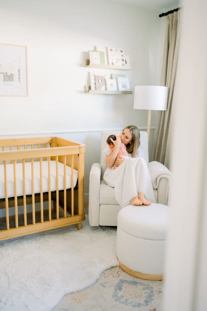 Mom kissing her newborn baby in his nursery while being photographed for his newborn photos.