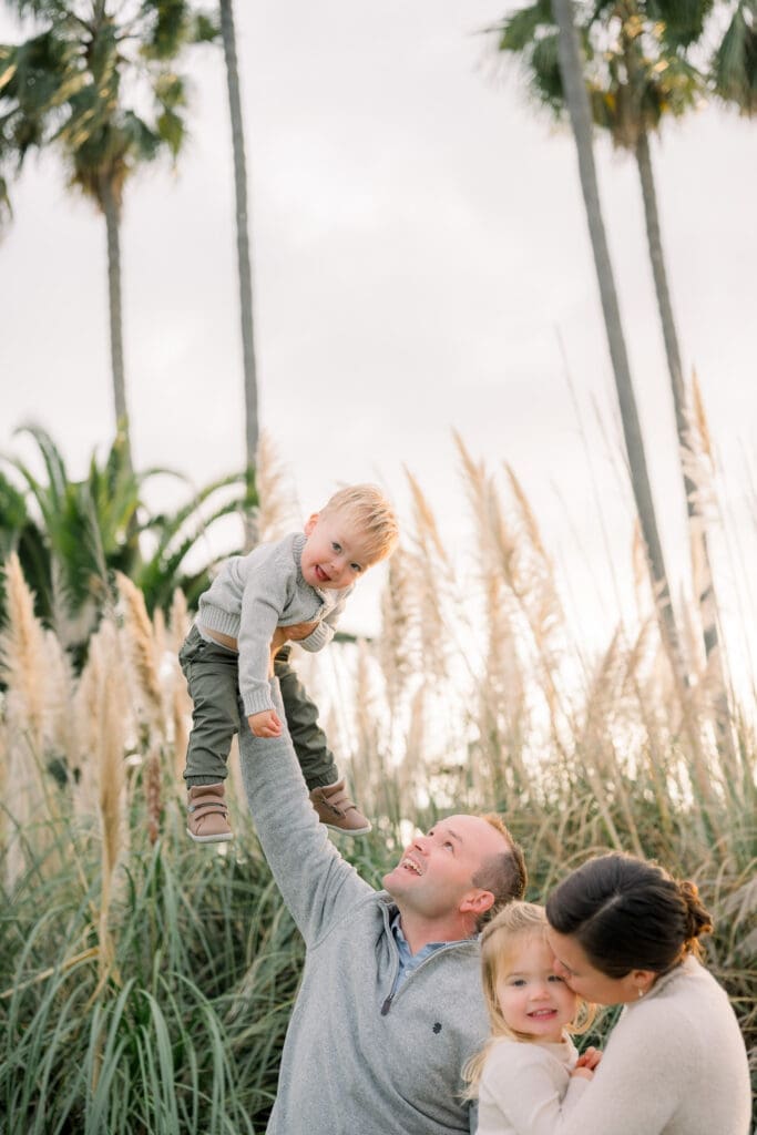 Dad holds his young son up in the air while mom and sister look on.