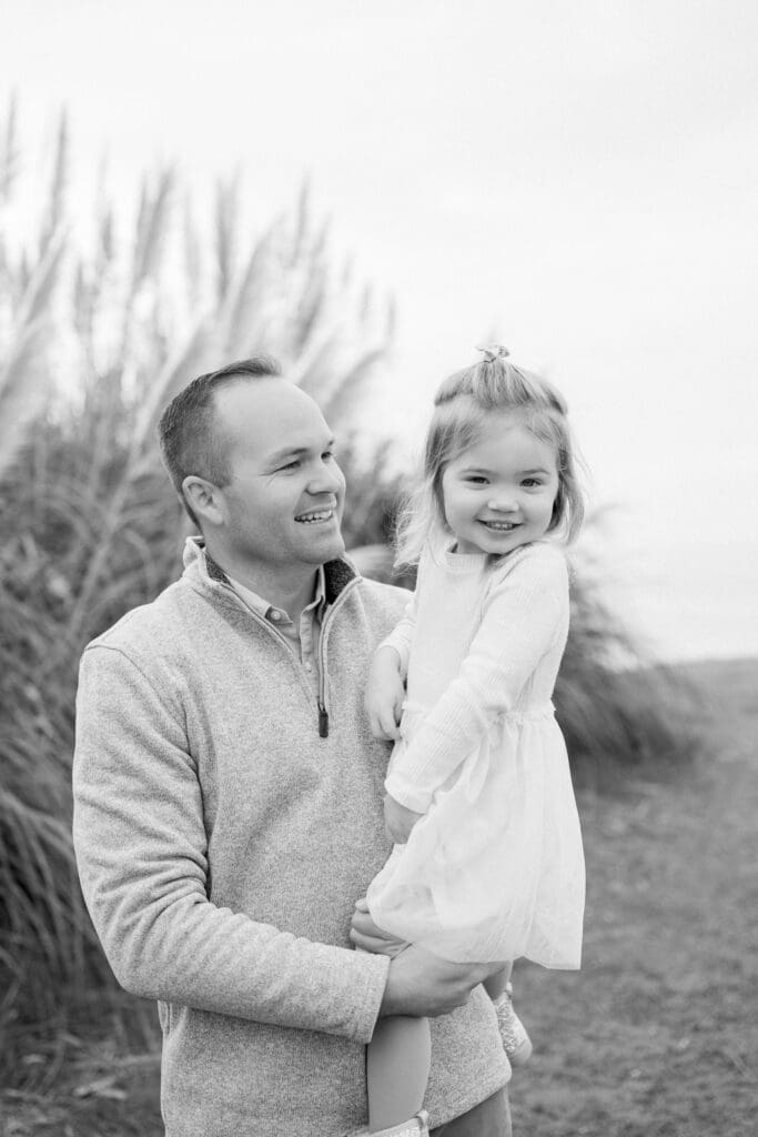 A dad holding his little girl and smiling while they take family photos at the Palos Verdes cliffs.