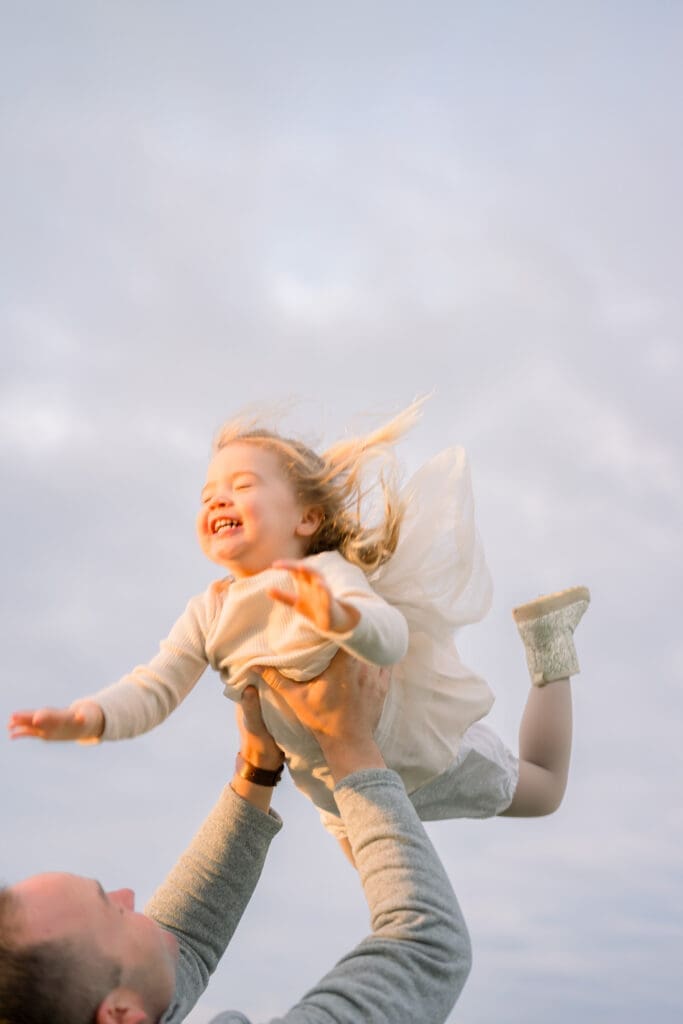 A little girl laughing while being tossed in the air by her dad as they take family photos in Palos Verdes.