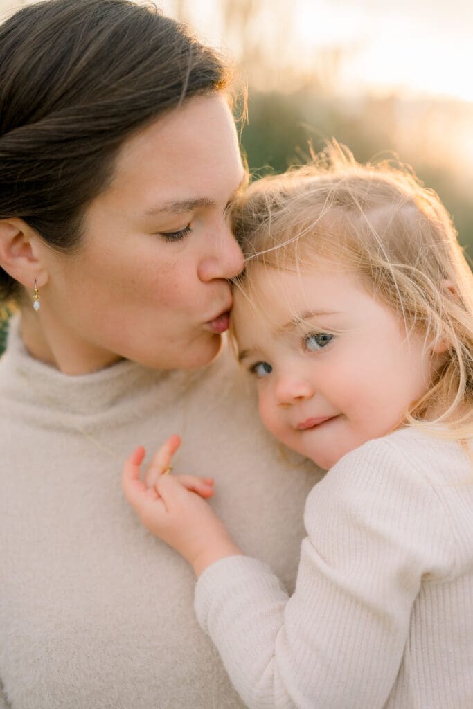 A mom kissing her little girl's head lovingly.